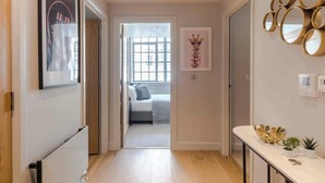 Un couloir avec un lit en arrière-plan, un miroir fixé au mur et un tableau encadré.