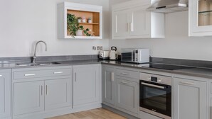 Une cuisine moderne avec des meubles gris, un four Bosch, un micro-ondes et une étagère intégrée pour les plantes.