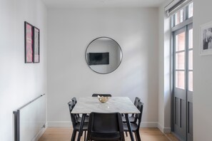 Un coin repas avec une table en marbre, des chaises noires, un miroir rond et des tableaux encadrés accrochés aux murs.