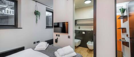 Une chambre d’hôtel moderne équipée d’un lit, d’une télévision, d’un miroir, d’une plante suspendue et offrant une vue sur l’extérieur.