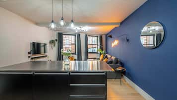 A modern kitchen with a central island, pendant lighting, a flat-screen TV, and a large mirror on the wall.