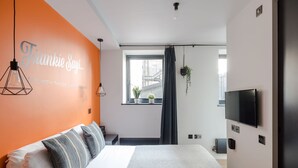 Ein modernes Hotelzimmer mit einem großen Bett, einem Fernseher und einer leuchtend orangefarbenen Wand mit einem Namen.