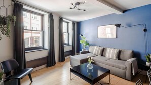 Ein modernes Wohnzimmer mit blauer Akzentwand, einem grauen Sofa, einem schwarzen Couchtisch und einem schwarzen Sessel.