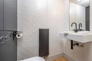 Ein Badezimmer mit weißen Fliesen, einem weißen Waschbecken, einem Spiegel und einer Toilette.