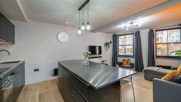 A modern kitchen with a central island, a dining area with a table, a sofa, and a TV.