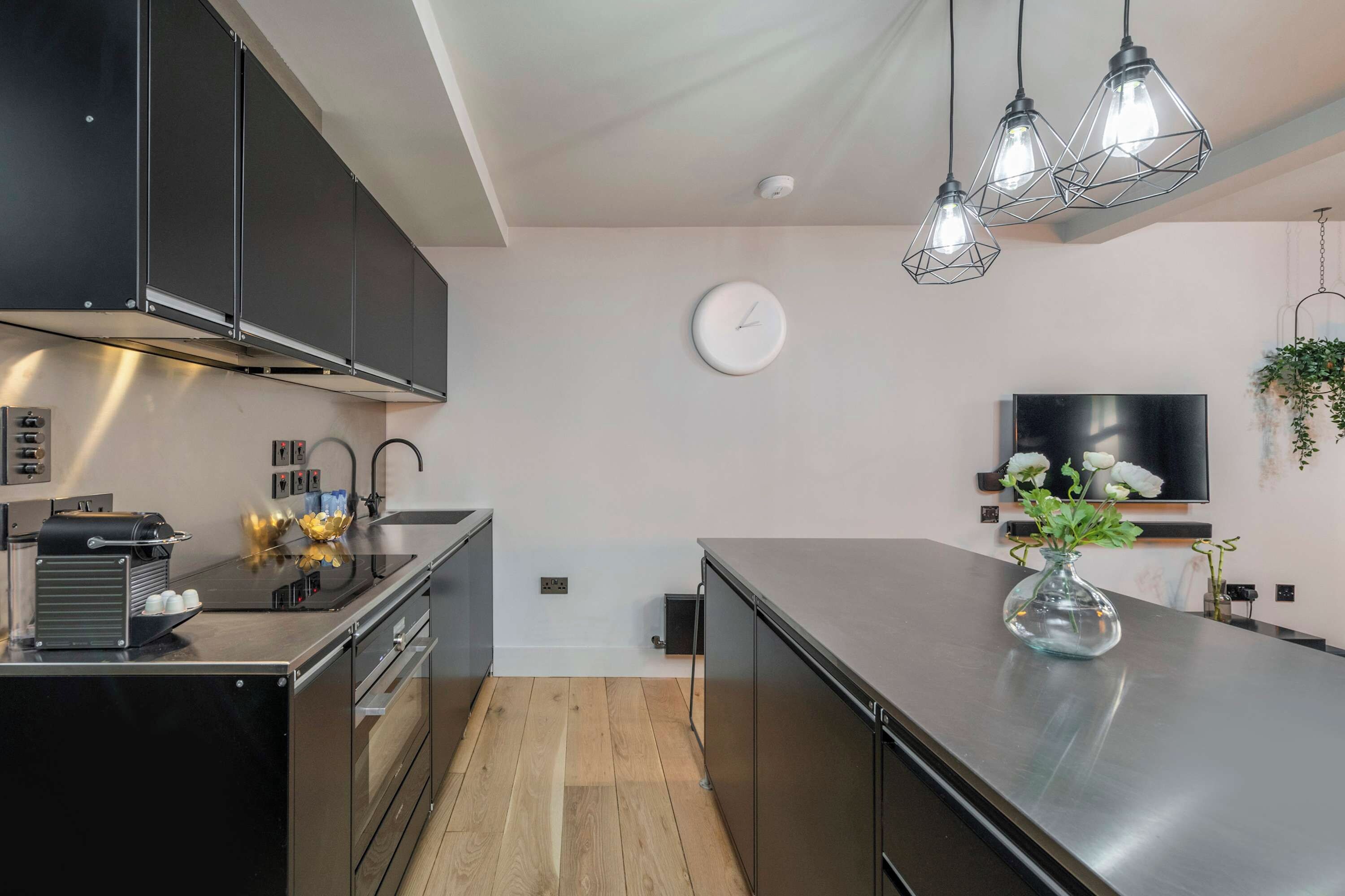 A modern kitchen with stainless steel appliances, a clock, and pendant lighting.