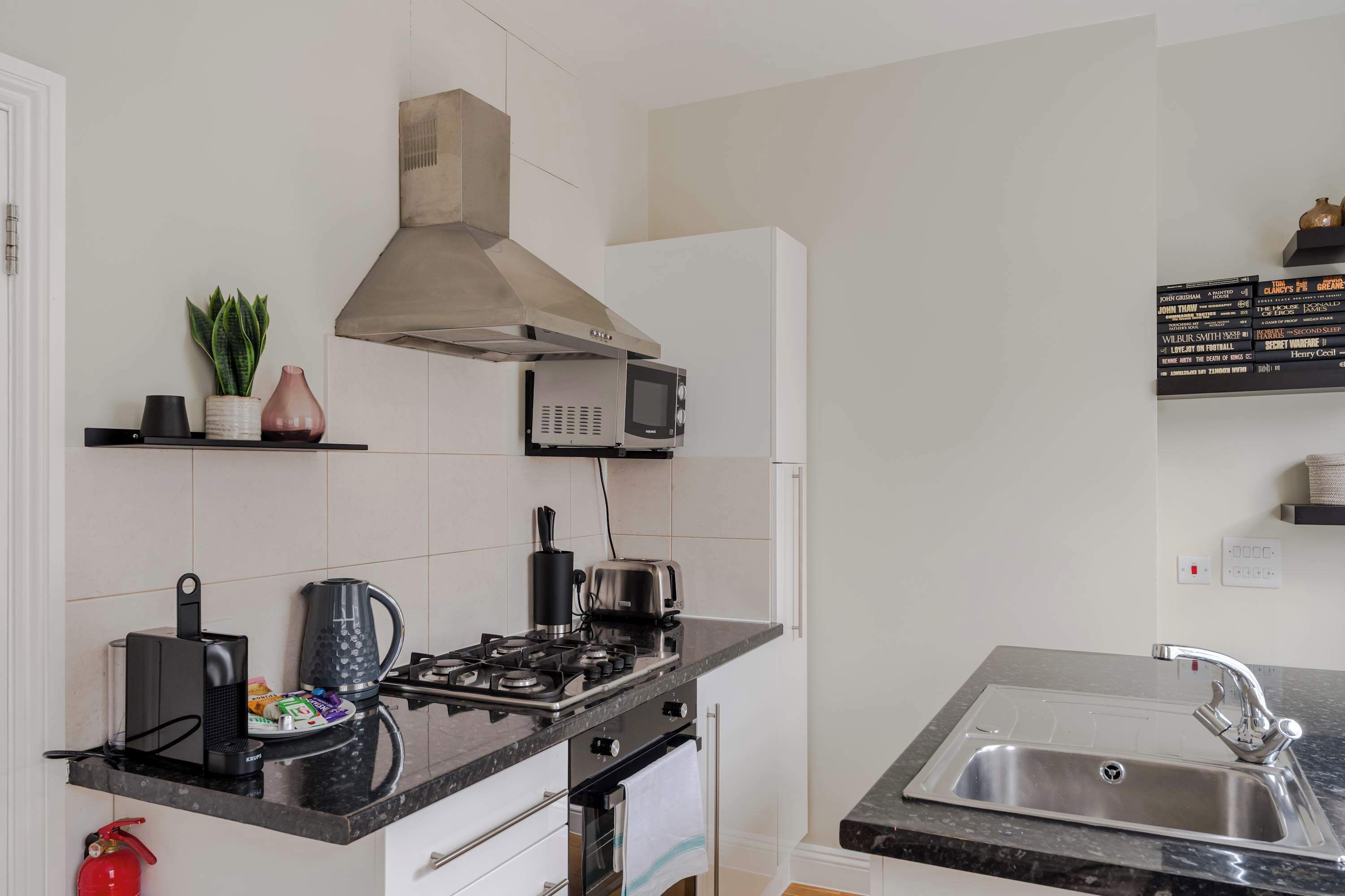 Cuina moderna amb fornet a gas, microones i bullidor. Hi ha un rentatamb vidre i una petita estantària amb objectes decoratius.