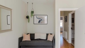 A modern living room with a grey sofa, a framed abstract painting, and a hanging plant. - The Lipstick Palace - Fitzrovia - by Frankie Says (London)