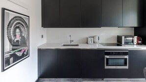 A modern kitchen with dark cabinets, a white countertop, a sink, a toaster, a kettle, a microwave, and an oven. - The Slaycation Crib: Stylish London Retreat By (London)