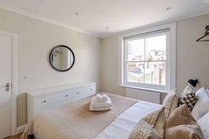 Een slaapkamer met een bed, een dressoir, een ronde spiegel, een raam met uitzicht op gebouwen en een radiator.
