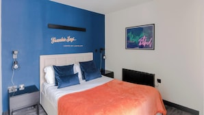 Un dormitorio con cama, mesitas de noche, una lámpara fijada a la pared y un cuadro enmarcado.