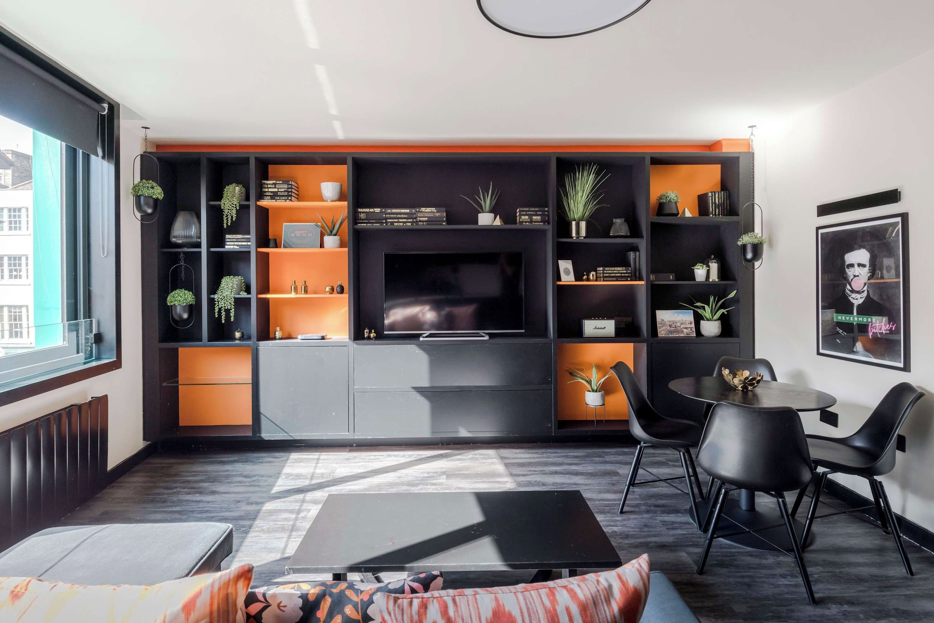 Een moderne woonkamer met een televisie, zwarte en oranje planken, een eethoek met stoelen, en een raam.