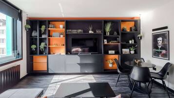 Een moderne woonkamer met een televisie, zwarte en oranje planken, een eethoek met stoelen, en een raam.