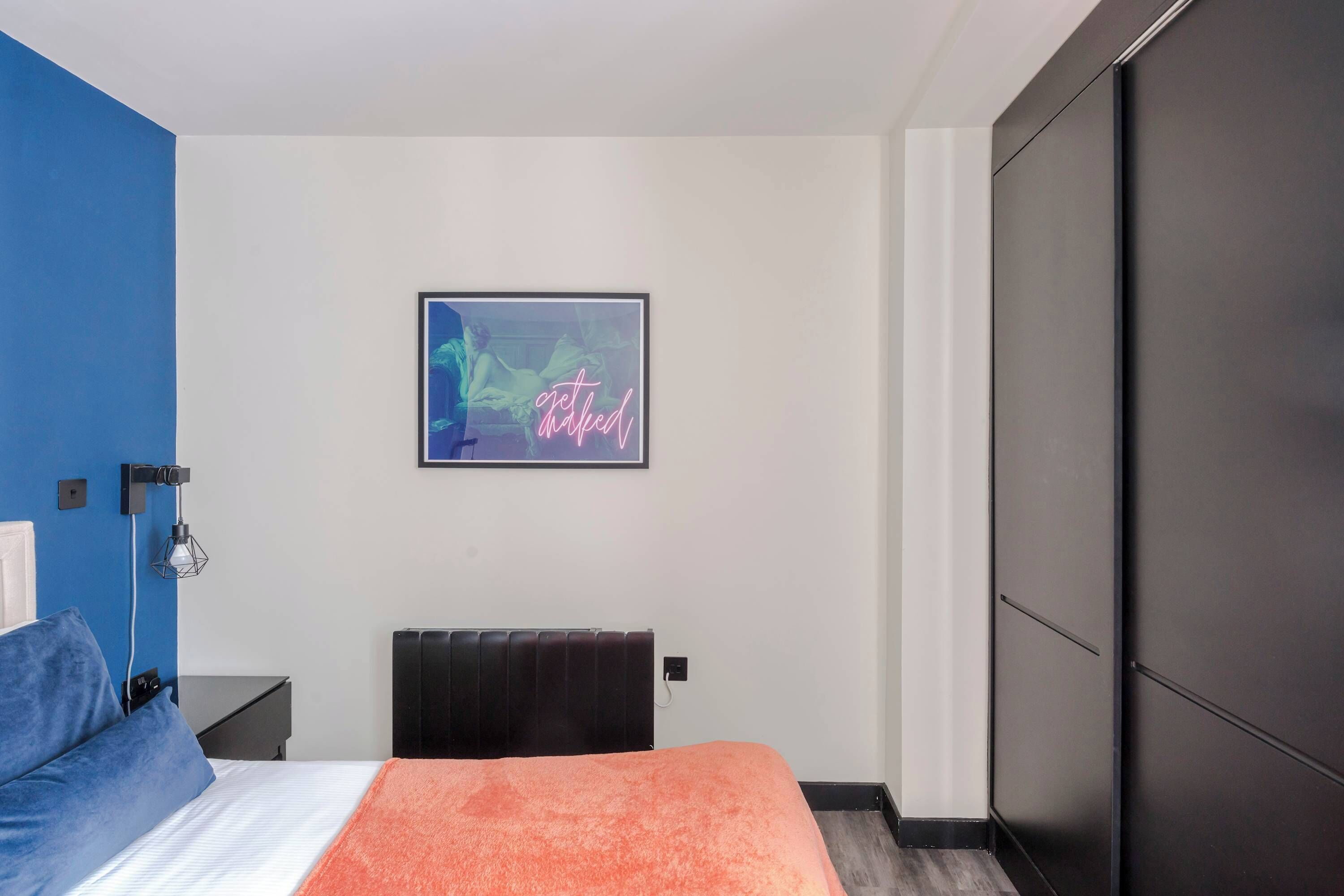 A modern bedroom with a bed, a nightstand, a wall-mounted lamp, a radiator, and a wardrobe.