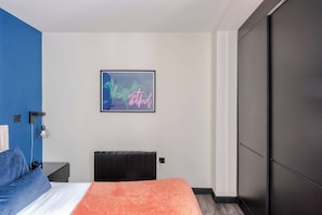 Une chambre à coucher moderne, avec un lit, une table de chevet, une lampe fixée au mur, un radiateur et une armoire.