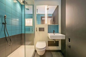 Une salle de bain moderne avec une douche à parois de verre, des toilettes blanches et un lavabo surmonté d’un miroir.