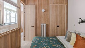 A bedroom with a wooden wardrobe, a radiator, and a bed with floral bedding. - The Italian Collection - Soho - by Frankie (London)