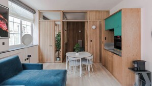 A modern kitchen with wooden cabinets, a dining area with a round table and chairs, and a blue sofa. - The Italian Collection - Soho - by Frankie (London)