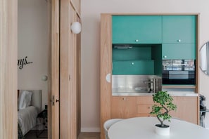 A compact kitchen with teal cabinets, a white countertop, and a small potted plant on a white table. - The Italian Collection - Soho - by Frankie (London)