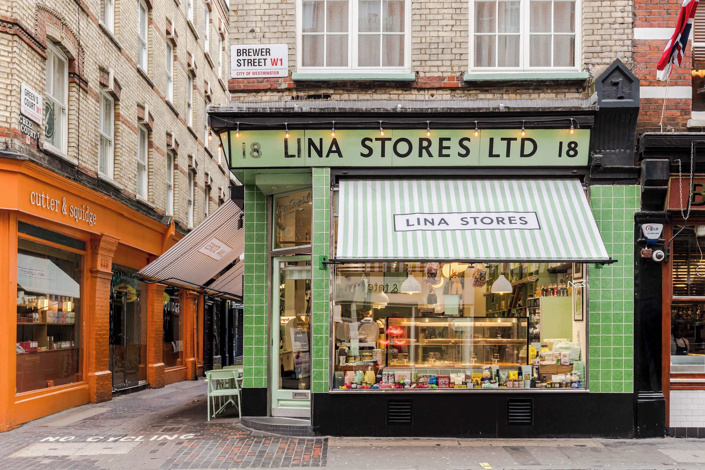 En butiksvindue med markise i grøn farve og et skilt, der siger 'LINA STORES LTD 18'.