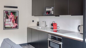 Una cucina moderna con mobili scuri, un lavello in acciaio inossidabile, un forno a microonde integrato, un bollitore rosso e un quadro appeso al muro.