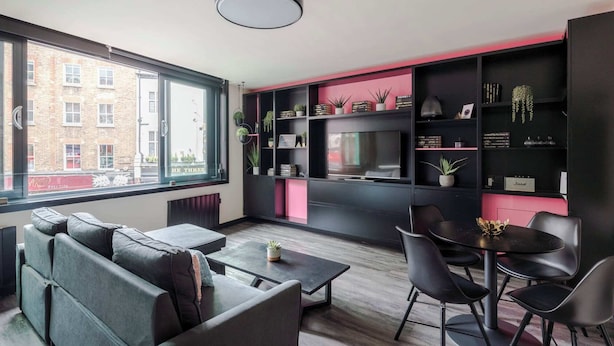 Un soggiorno moderno con divano, tavolino da caffè e zona pranzo. È presente una grande finestra con vista sugli edifici.