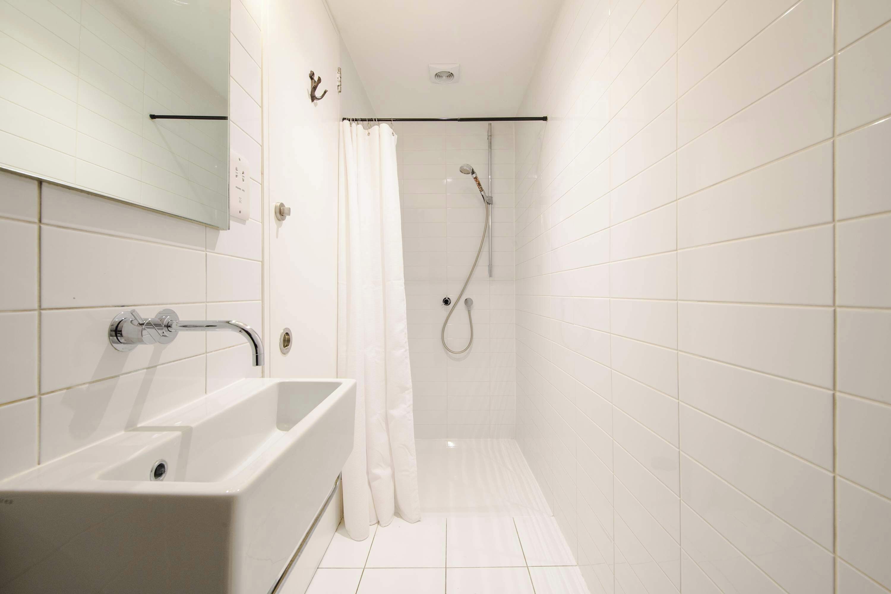 Uma casa de banho com uma banheira branca, um chuveiro com chuveiro manual e um chão em azulejos brancos.