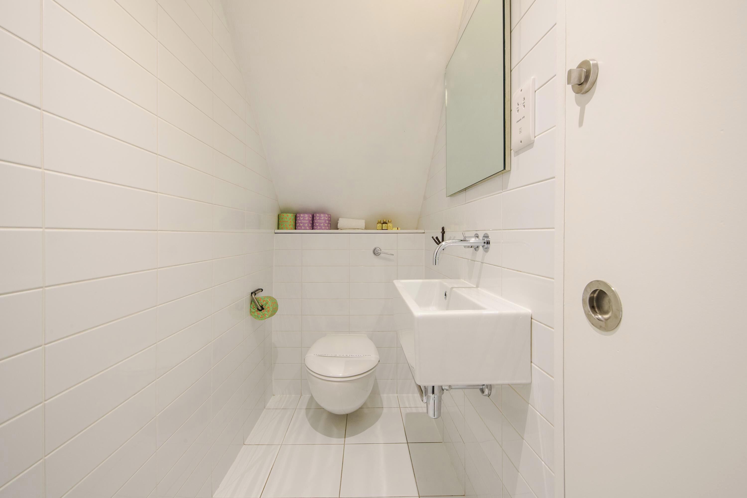 Une petite salle de bain moderne avec des carreaux blancs, des toilettes, un lavabo et un miroir.