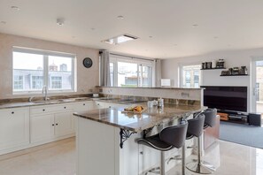 Una cocina moderna con una isla grande, taburetes de bar y un área de comedor con televisor.