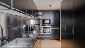 A modern kitchen with stainless steel appliances, a large sink, and wooden flooring. - The Acre Penthouse - Covent Garden - by Frankie (London)