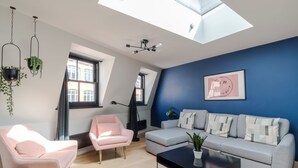 A modern living room with a blue accent wall, a grey sofa, a pink armchair, and a black coffee table. - The Acre Penthouse - Covent Garden - by Frankie (London)