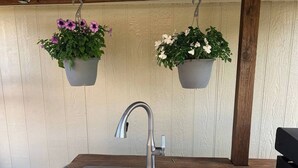 A kitchen with a double stainless steel sink, wooden countertop, and hanging flower pots with purple and white flowers. - Saykm Bungalow Lake Texoma walking distance to sandy beach & boat ramp (Pottsboro)