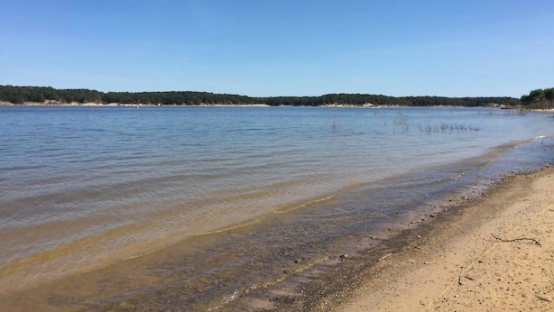 A beach with clear water, sandy shore, and a forested background. - Saykm Bungalow Lake Texoma walking distance to sandy beach & boat ramp (Pottsboro)