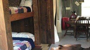 A rustic room with a bunk bed, a dining area with a red table and chairs, a ceiling fan, and a cowhide rug. - Saykm Bungalow Lake Texoma walking distance to sandy beach & boat ramp (Pottsboro)