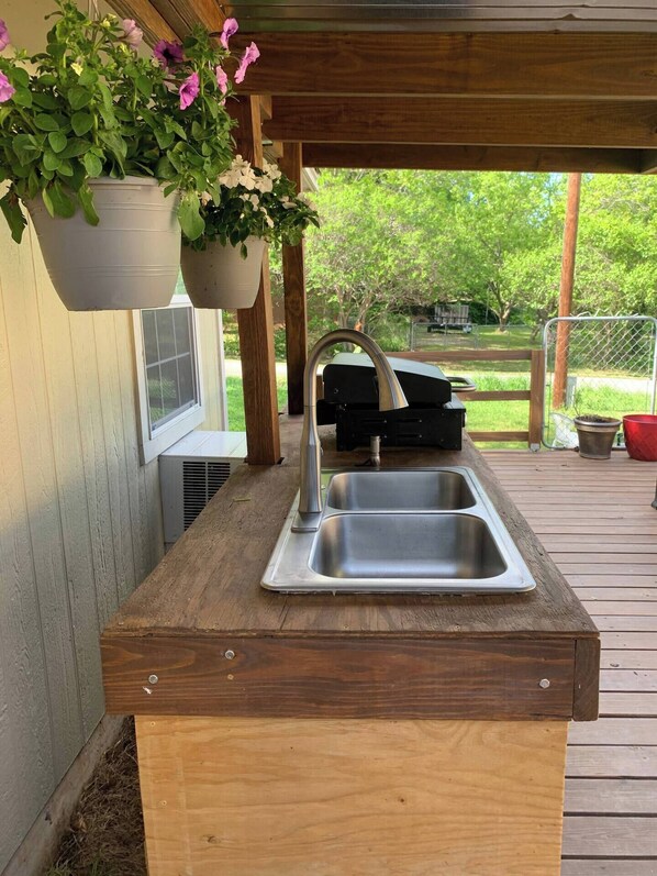 Una terraza de madera con un lavamanos integrado y macetas colgantes.