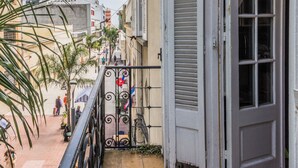 Un corridoio esterno stretto con ringhiera in metallo, una porta con persiane e pavimento piastrellato.