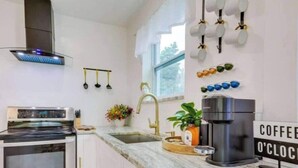A kitchen with a modern stove, a sink, and a coffee machine. There is a window with a view of trees and a sign that says "COFFEE O'CLOCK". - Wynwood Escape
Built for long-term stay (Miami)