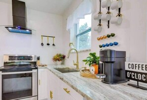 A kitchen with a modern stove, a sink, and a coffee machine. There is a window with a view of trees and a sign that says "COFFEE O'CLOCK". - Wynwood Escape
Built for long-term stay (Miami)