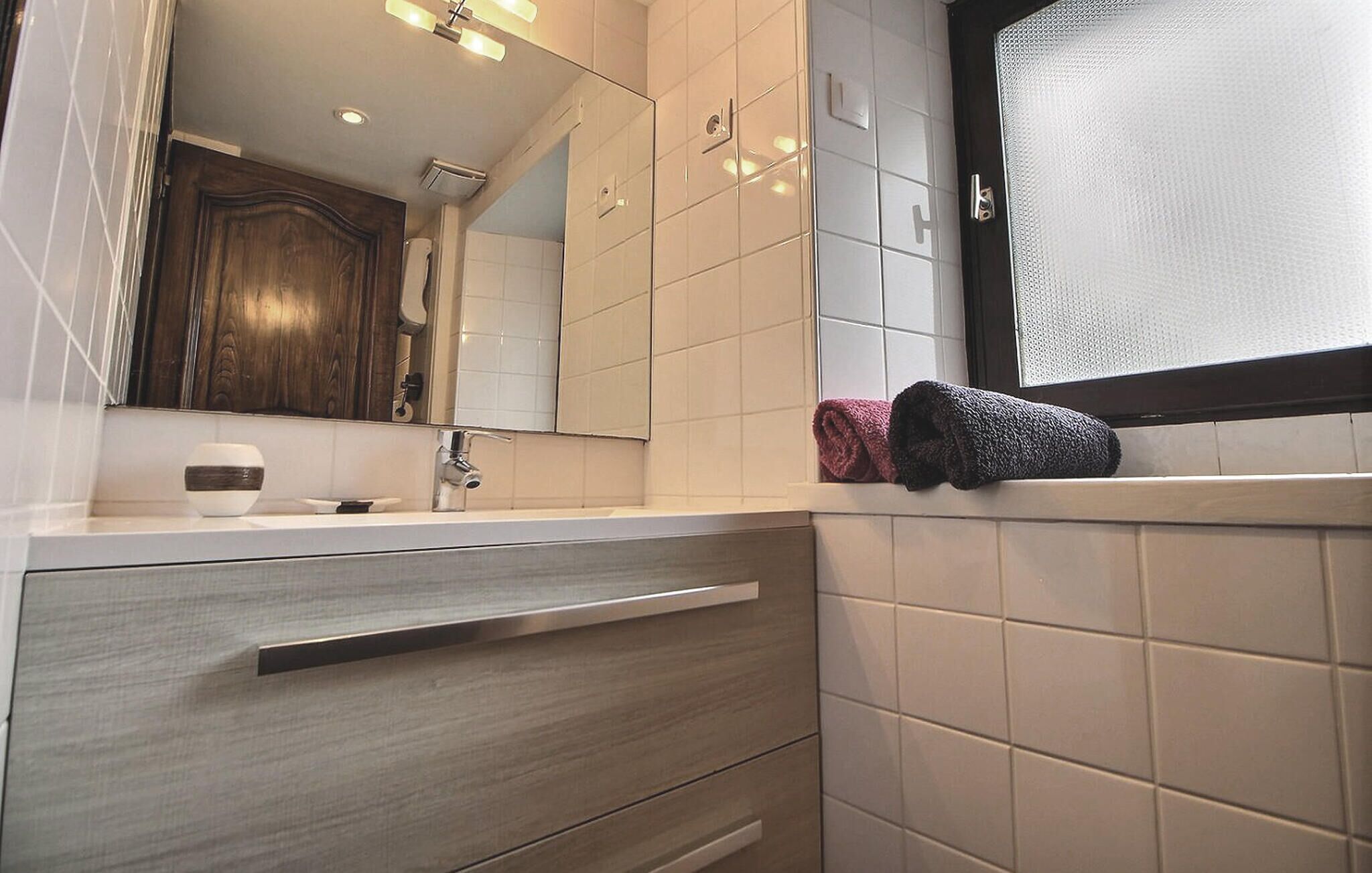 A modern bathroom with a wooden vanity, a mirror, a towel rack, and a window with a textured blind.
