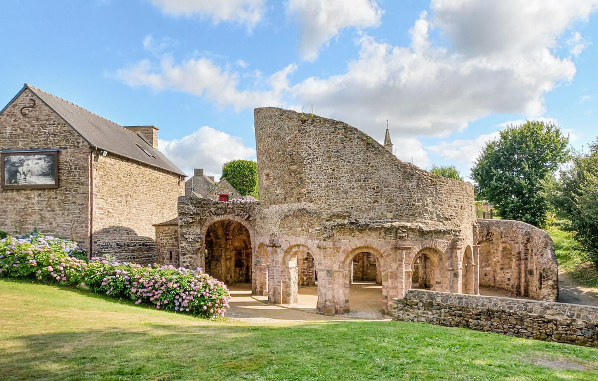 A stone building with a large arched entrance, a smaller arched structure, and a garden with flowers.