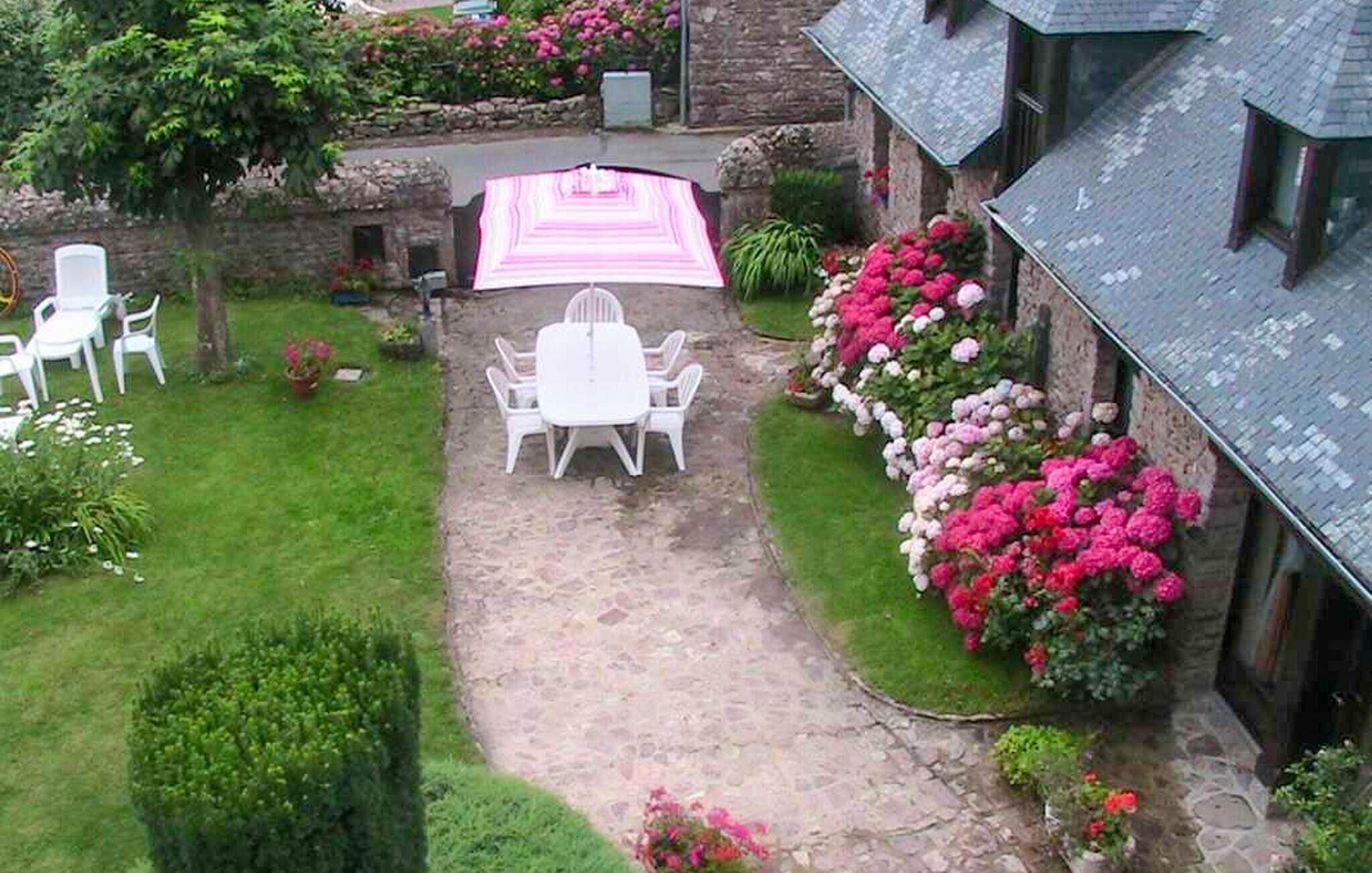 Een pad van stenen leidt naar een wit zitgedeelte buiten, met een gestreept vloerkleed, omgeven door weelderige begroeiing en bloeiende planten.