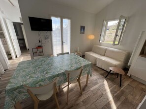 A room with a dining table, chairs, a sofa, a TV, and a window. - 148 – Charming House with Large Garden – Ideal for 4 to 6 Guests ?? (SOULAC SUR MER)
