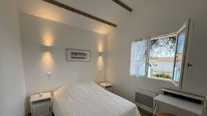 A bedroom with a bed, bedside tables, a desk, and a window. - 148 – Charming House with Large Garden – Ideal for 4 to 6 Guests ?? (SOULAC SUR MER)