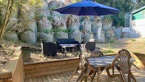 A wooden deck with a table and chairs, a blue umbrella, and outdoor furniture. - 148 – Charming House with Large Garden – Ideal for 4 to 6 Guests ?? (SOULAC SUR MER)