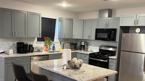 A modern kitchen with grey cabinets, a stainless steel refrigerator, a microwave, and a granite countertop. - Cozy 3-bedroom house in perfect Newark with cool AC/HEAT and comfort (Newark)