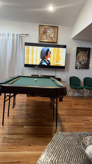 A room with a pool table, a television mounted on the wall, and two green chairs. - Cozy 3-bedroom house in perfect Newark with cool AC/HEAT and comfort (Newark)