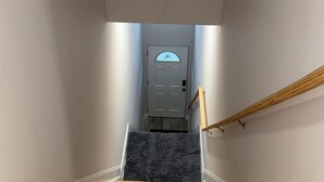 A wooden staircase with a handrail leading to a door with a frosted glass window. - Cozy 3-bedroom house in perfect Newark with cool AC/HEAT and comfort (Newark)