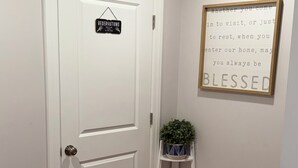 A white door with a 'RESERVATIONS' sign, a small shelf with a plant, and a framed inspirational quote on the wall. - Cozy 3-bedroom house in perfect Newark with cool AC/HEAT and comfort (Newark)
