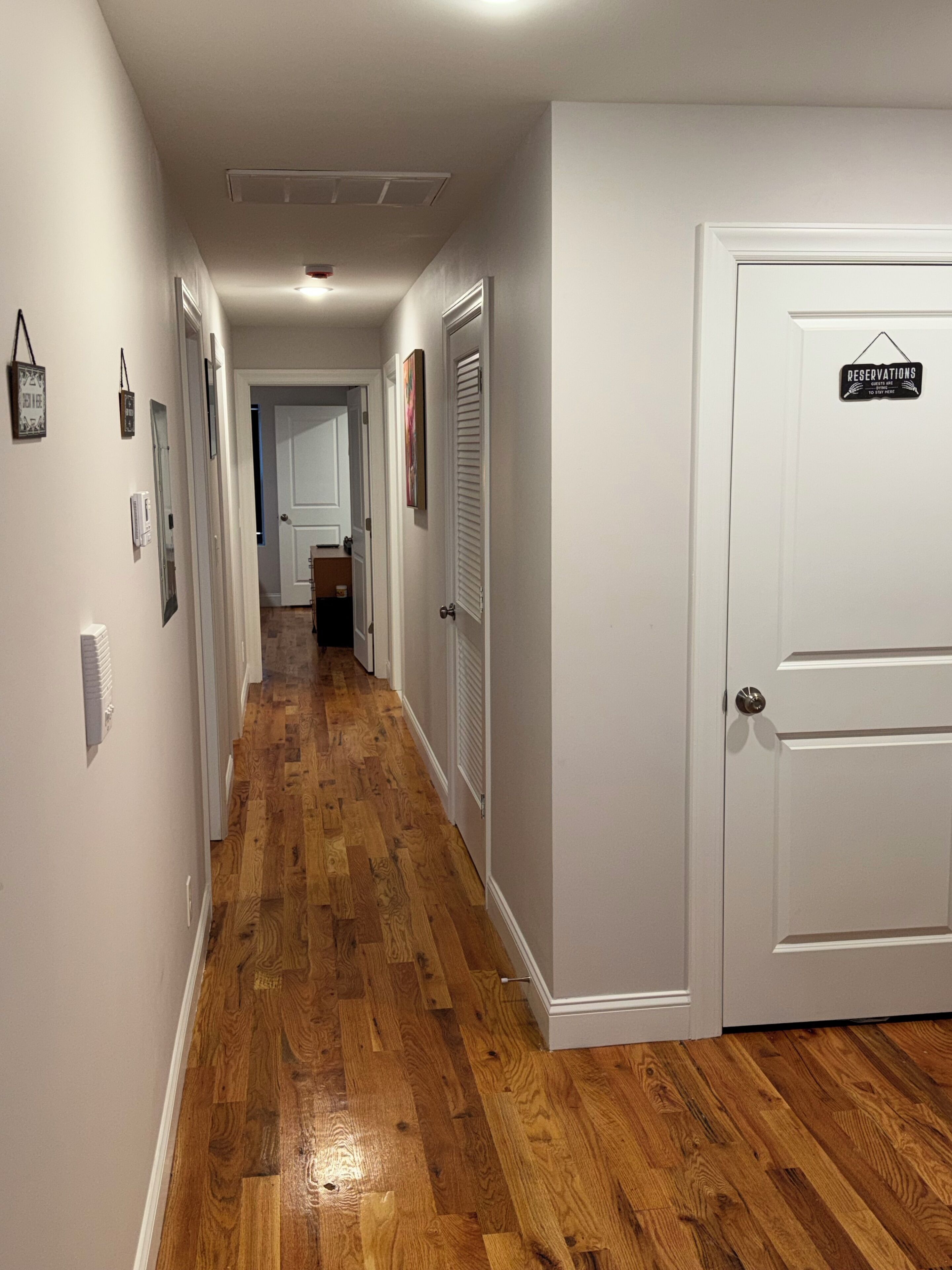 A hallway with wooden flooring, white walls, and a door with a 'Reservations' sign.