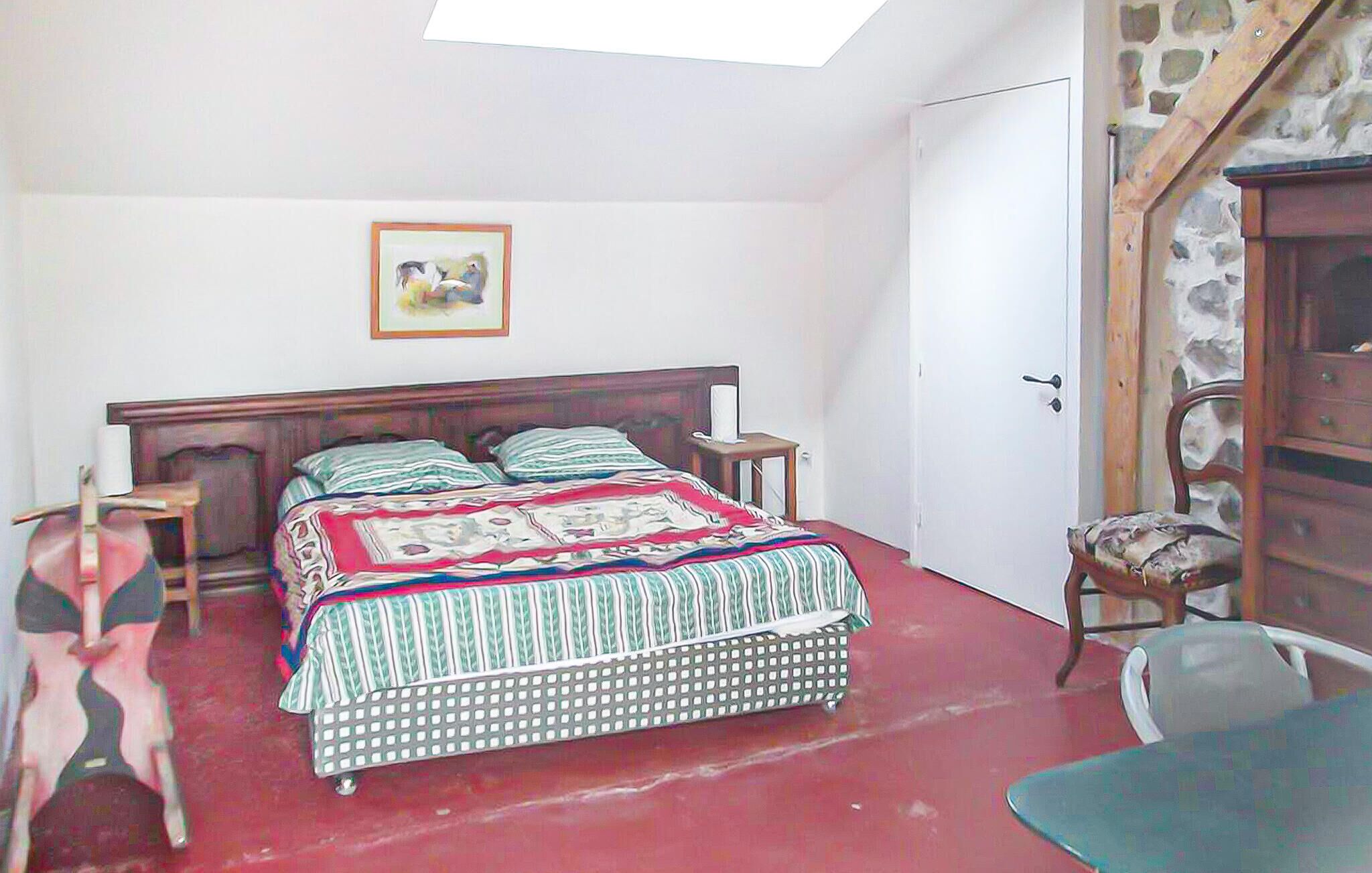 Un dormitorio con una cama, una mesita de noche, una silla, un armario de madera y una pared de piedra.